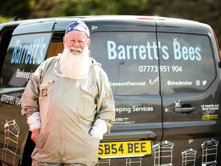 Person in beekeeping suit stands next to a van labeled 